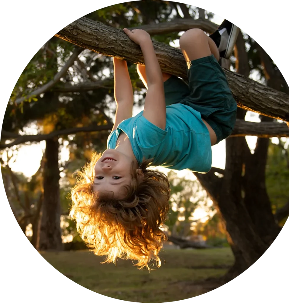 Child climbing a tree outside and hanging upside-down off a branch