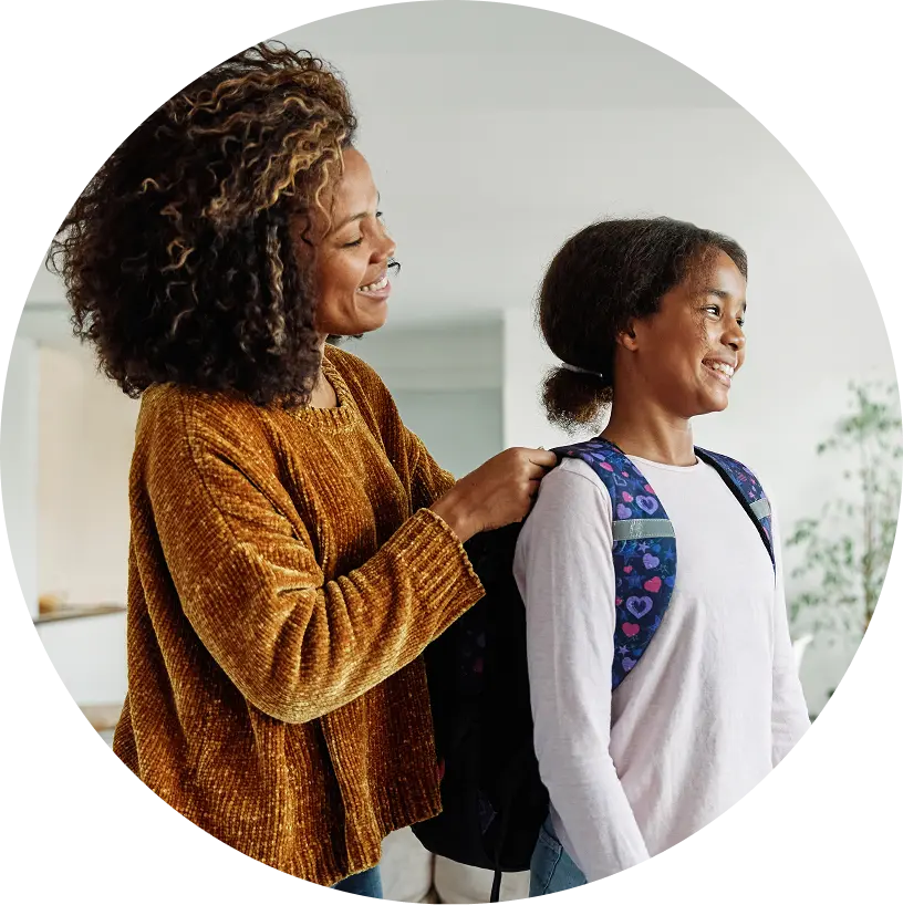 Mom helping her daughter put her backpack on in their living room