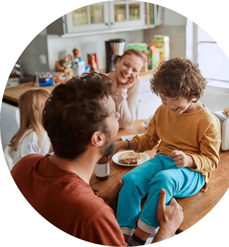 Family laughing at the kitchen table while eating breakfast